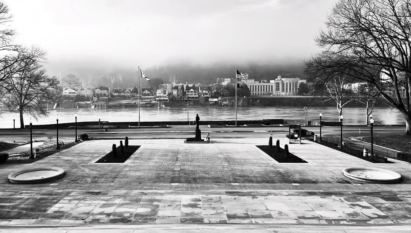 Black and white view of Kanawha Boulevard and river from Capitol steps, featuring flags and morning fog.